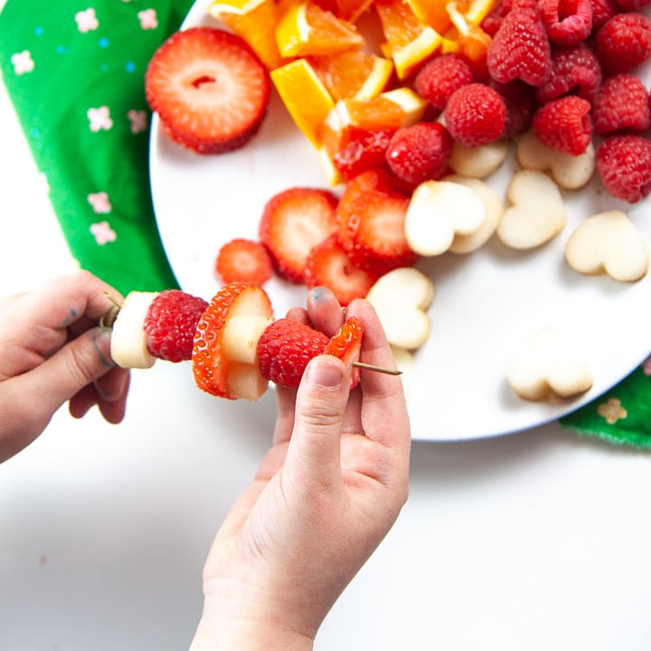 Small kid hands making their own fruit sticks for drink