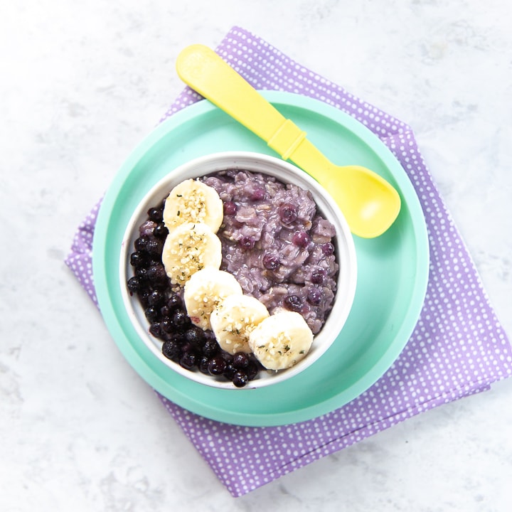 Bowl filled with blueberry oatmeal with slices of banana and frozen blueberries on top.