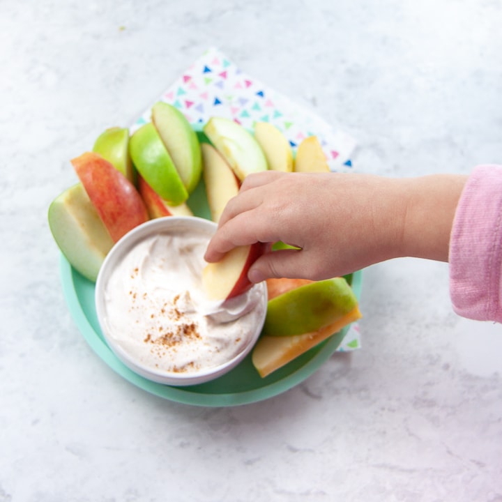 Toddler hands dipping an apple into healthy spiced dip.
