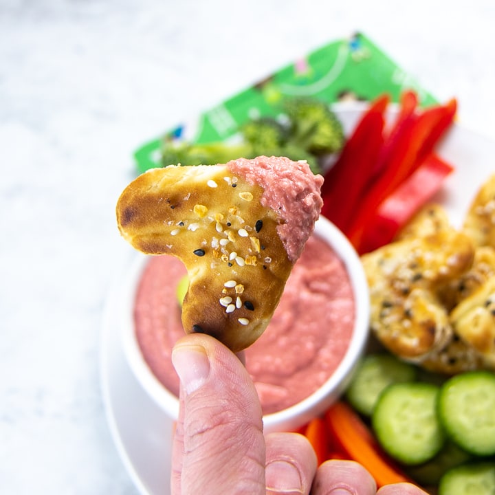 heart pita bread dipped into beet hummus with plate of veggies
