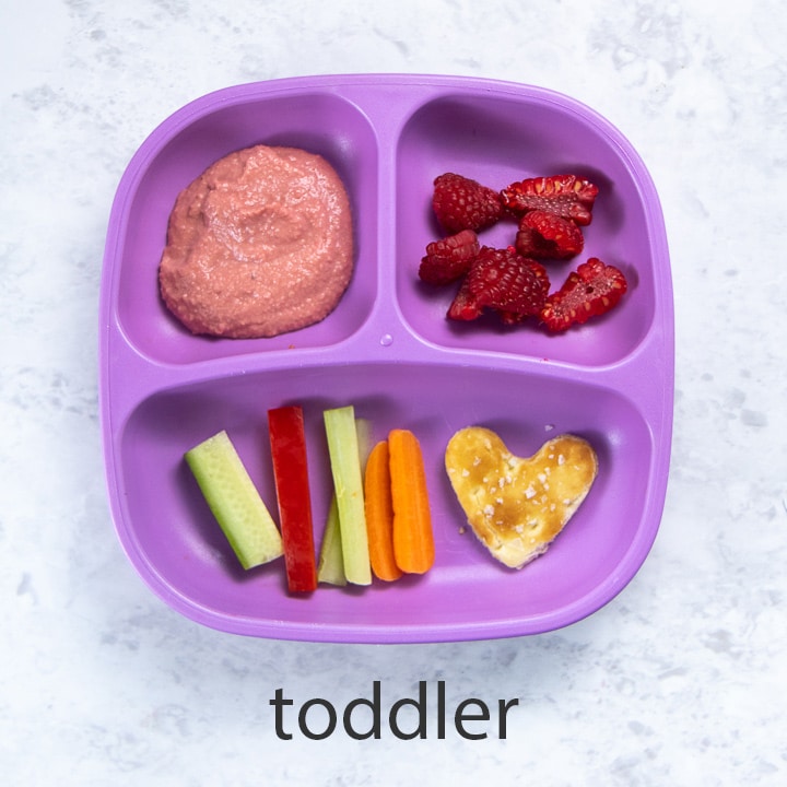purple toddler plate filled with beet hummus, veggies and snacks.
