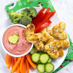 bowl of beet hummus with plate full of chopped veggies and cut-out heart pita bread.