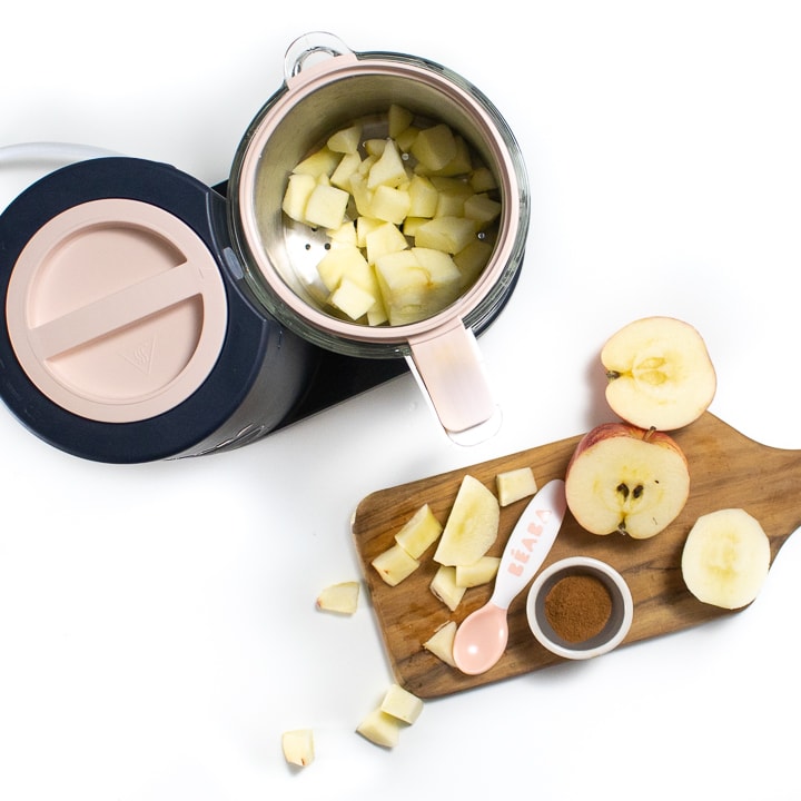 Spread of Beaba babycook and a cutting board with raw apples in chunks with a small bowl of cinnamon.