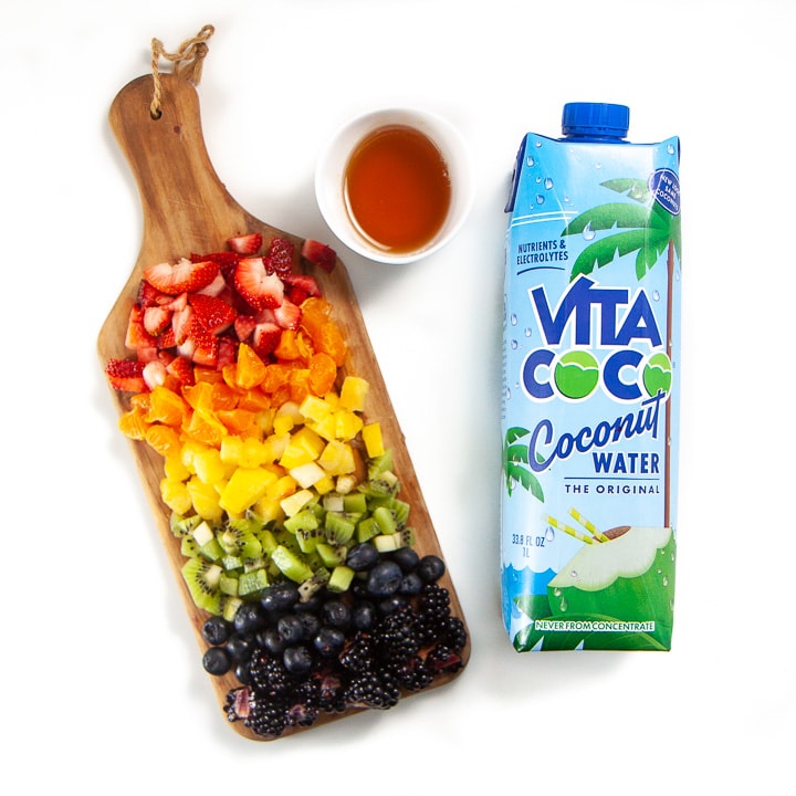 Cutting board with rainbow fruit, coconut water and honey for popsicles for toddler and kids.
