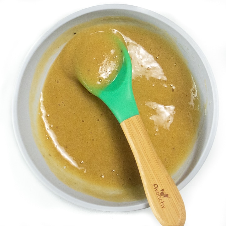 Bowl full of banana and peach puree with baby spoon in it.