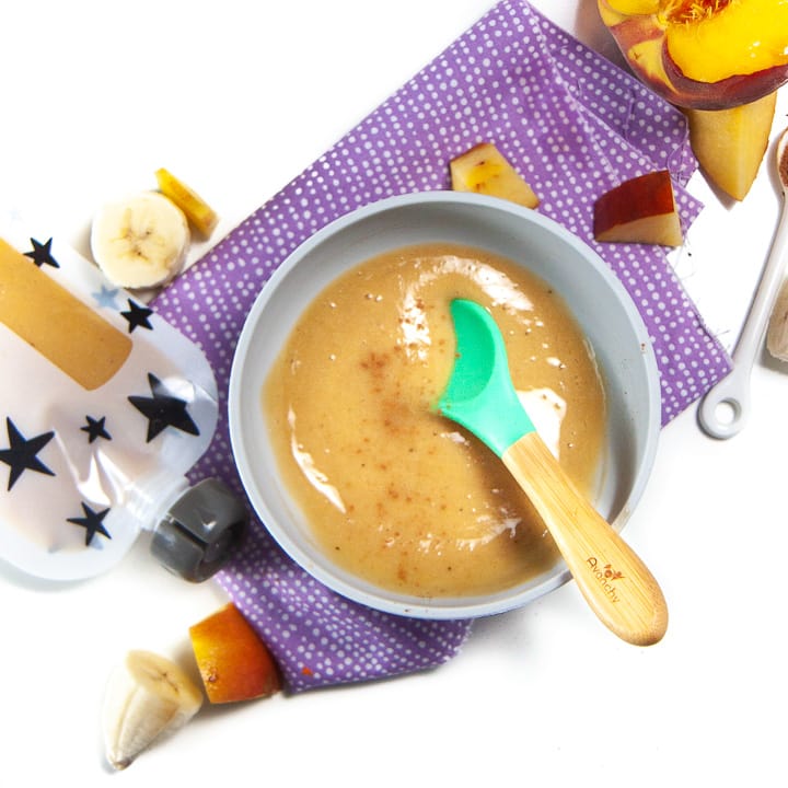 Bowl full of peach and banana puree for baby with food around the bowl.
