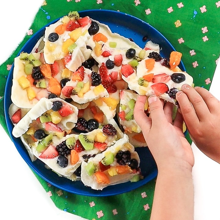small kid hands reaching into a pile of bark to grab a piece of frozen yogurt bark.