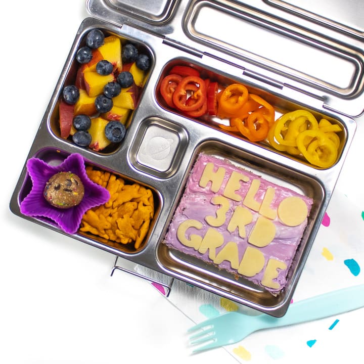 A silver bento school lunch box with a fun and colorful lunch for the first day of school.