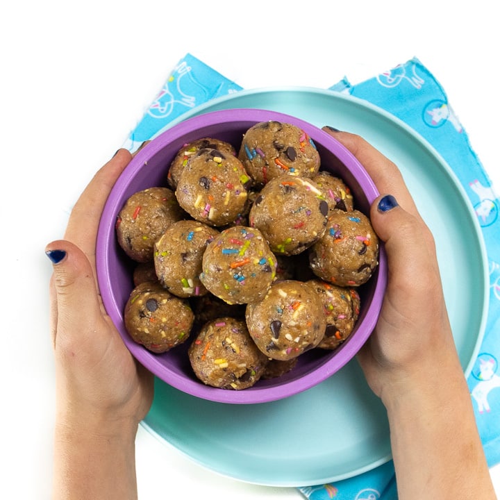Small kids hands holding a bowl of funfetti energy balls. 