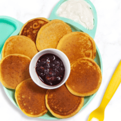 kids blue bear plate on a kitchen marble counter with a bunch of sweet potato pancakes on it with a berry sauce and yogurt.