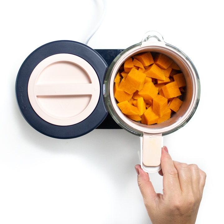 Hand holding the glass jar of a babycook with steamed veggies inside.