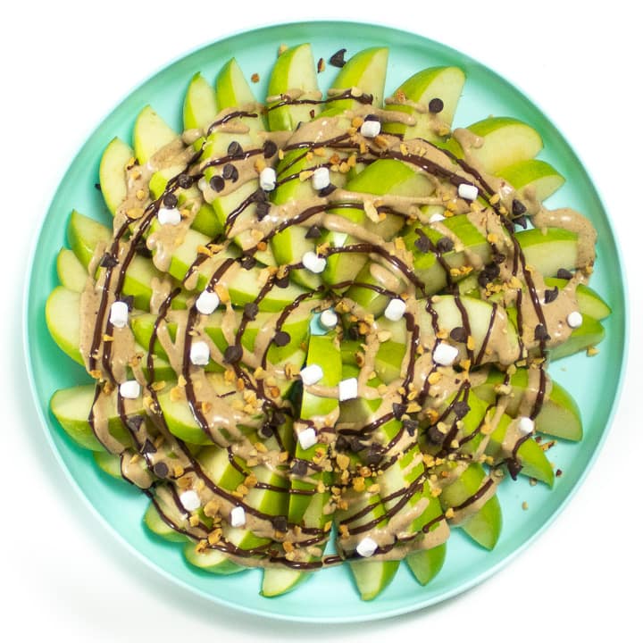 Plate with apple nachos with healthy caramel, melted chocolate and topping.