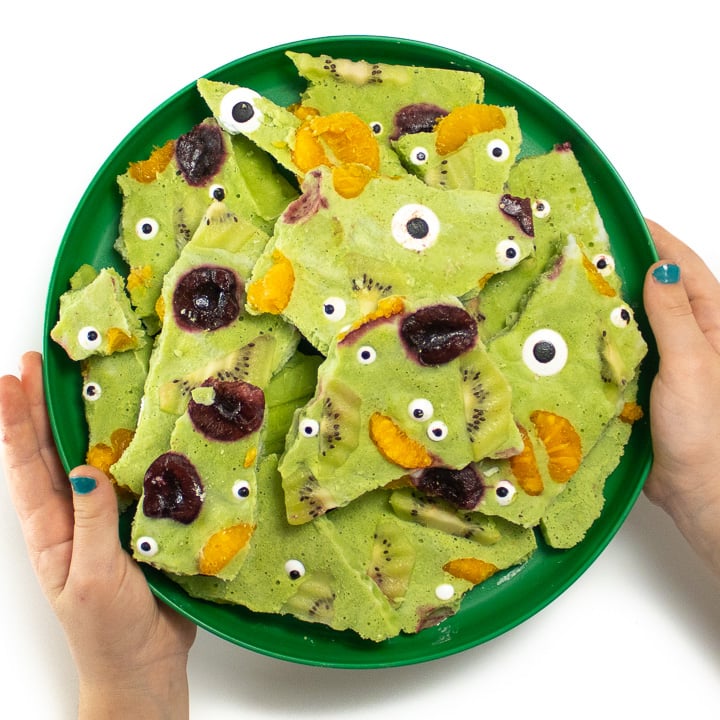 Small hands holding a plate of monster frozen yogurt bark.