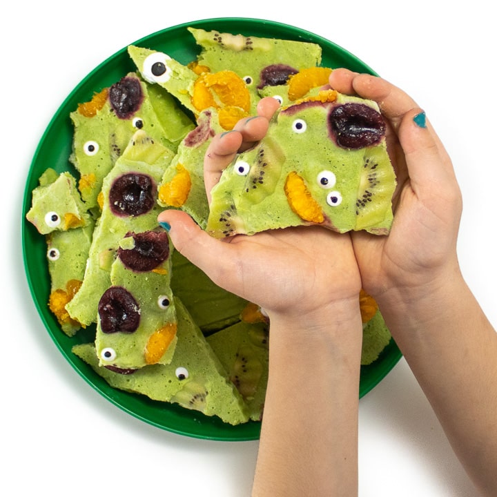 Small kids hands holding a piece of yogurt bark for halloween.
