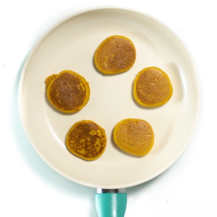 5 pancakes cooking on a pan.
