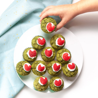 Small hand grabbing a green grinch mini muffin.