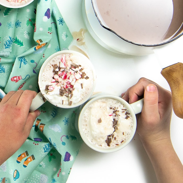 2 hands grabbing mugs of hot chocolate.