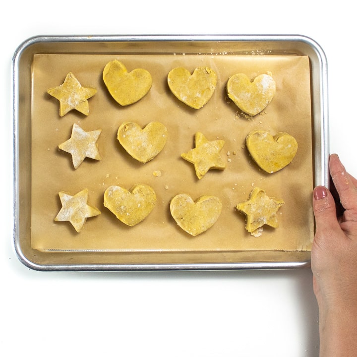 Hand holding a small baking sheet full of heart and star shaped pumpkin biscuits for kids.