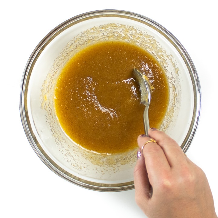 Hand stirring a bowl filled with melted butter and sugar.