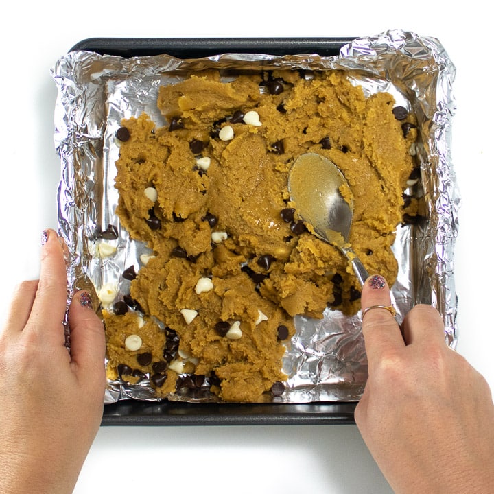 Hands pressing down the cookie dough into the pan.