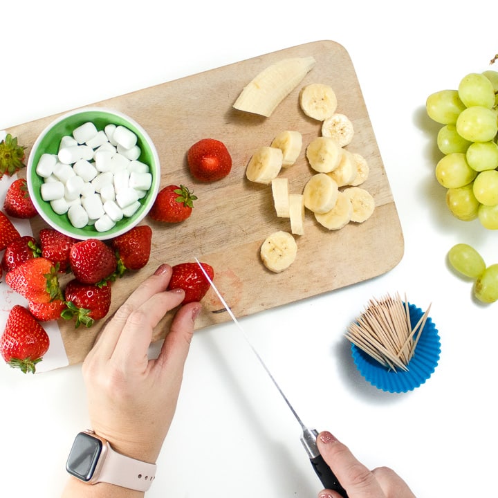 Hands cutting the tops of the strawberries off.