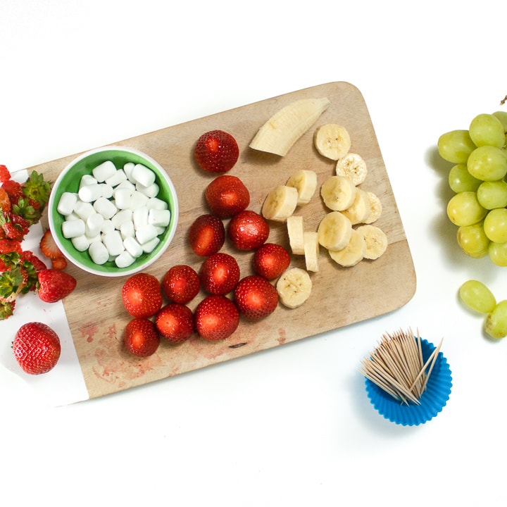 Cutting board with strawberries, cut bananas and marshmallows.
