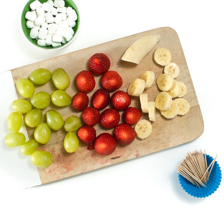 Cutting board with grapes, strawberries and sliced bananas for fruit kabobs.