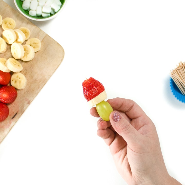 Hands holding a fruit pick grape, banana and strawberry on it.