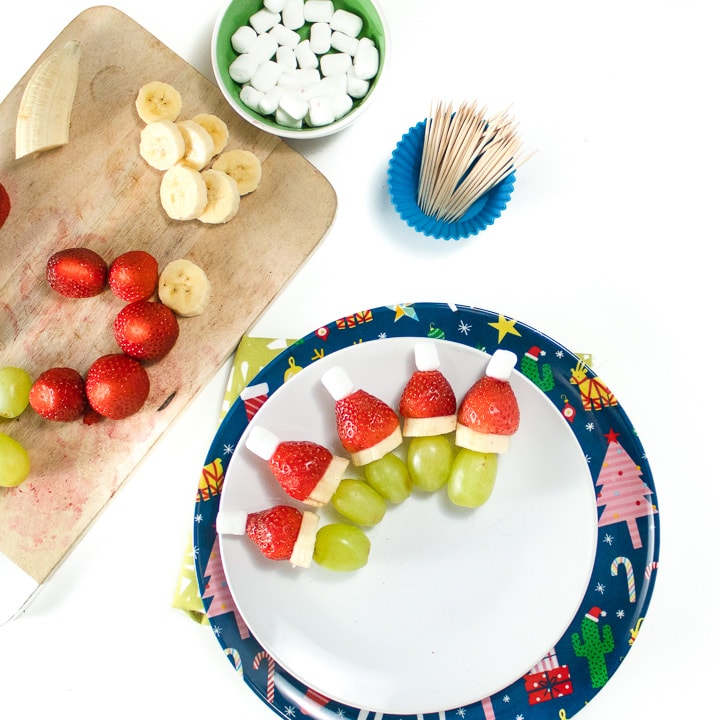 Cutting board with ingredients being assemble for grinch kabobs.