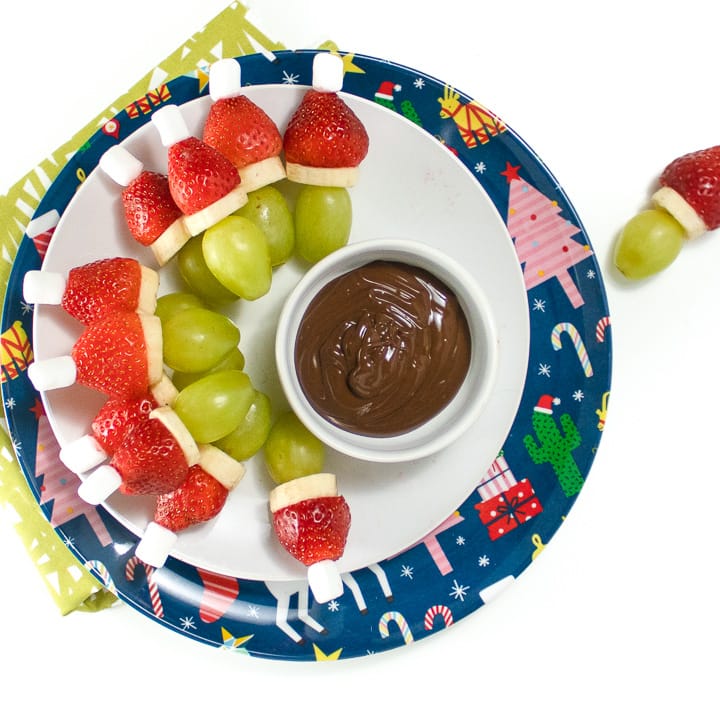 Round plate with grinch fruit kabobs on it.
