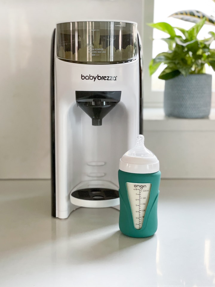 Glass bottle sitting in front of a baby Brezza advanced formula pro machine.
