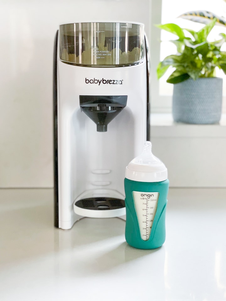 Glass bottle sitting in front of a baby Brezza advanced formula pro machine.