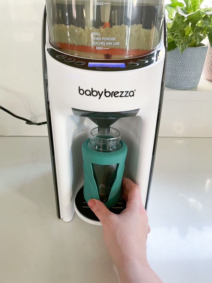 Hand holding a bottle while it is filling up under the baby Brezza.