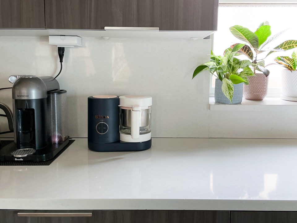 Black Beaba babycook on a white counter with a coffee machine and plant.