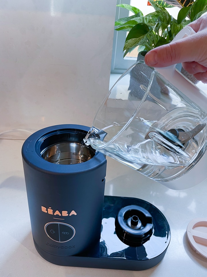 Hand pouring water into the Beaba tank.