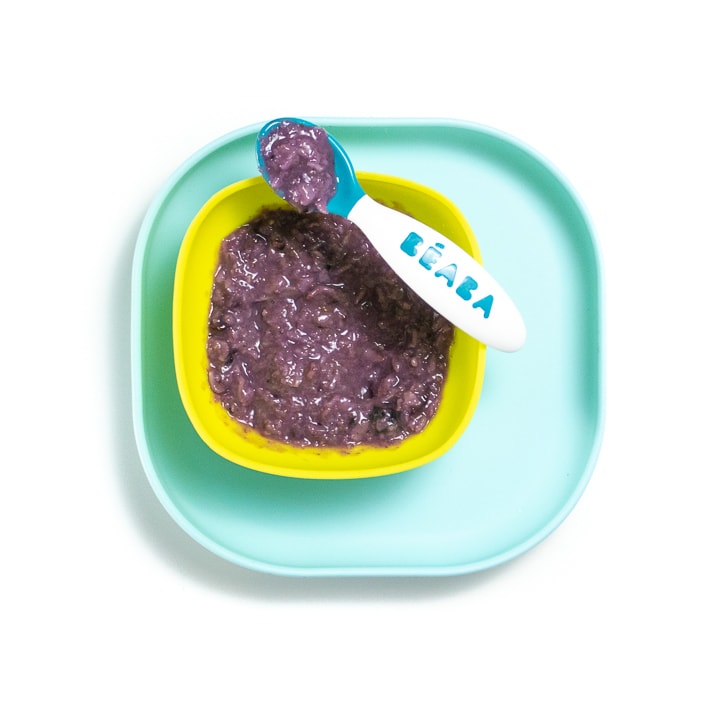 Teal plate with green bowl with purple blueberry oatmeal inside.