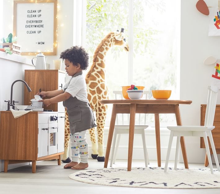 Kid playing at a kitchen toy that is wood and white.