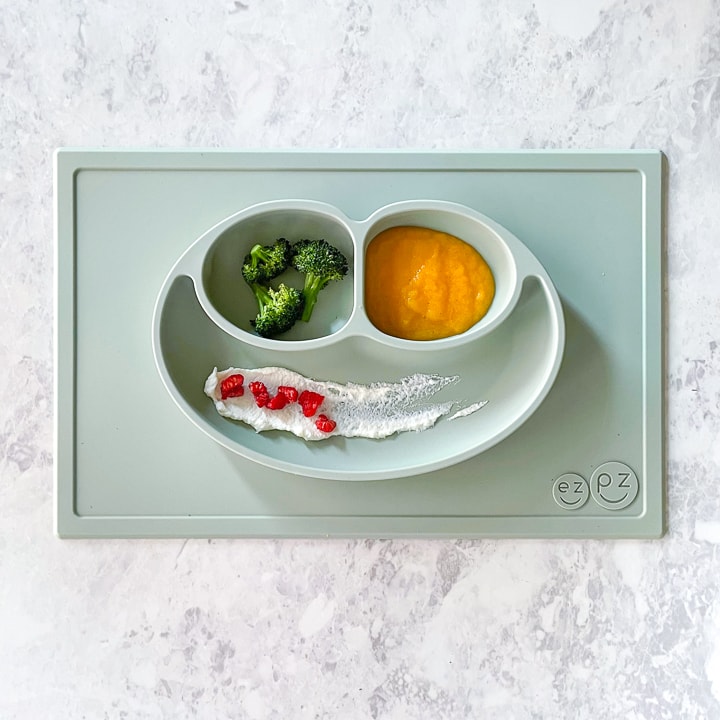 sage ezpz mat on a marbled counter with broccoli, peach puree and ricotta with raspberries.