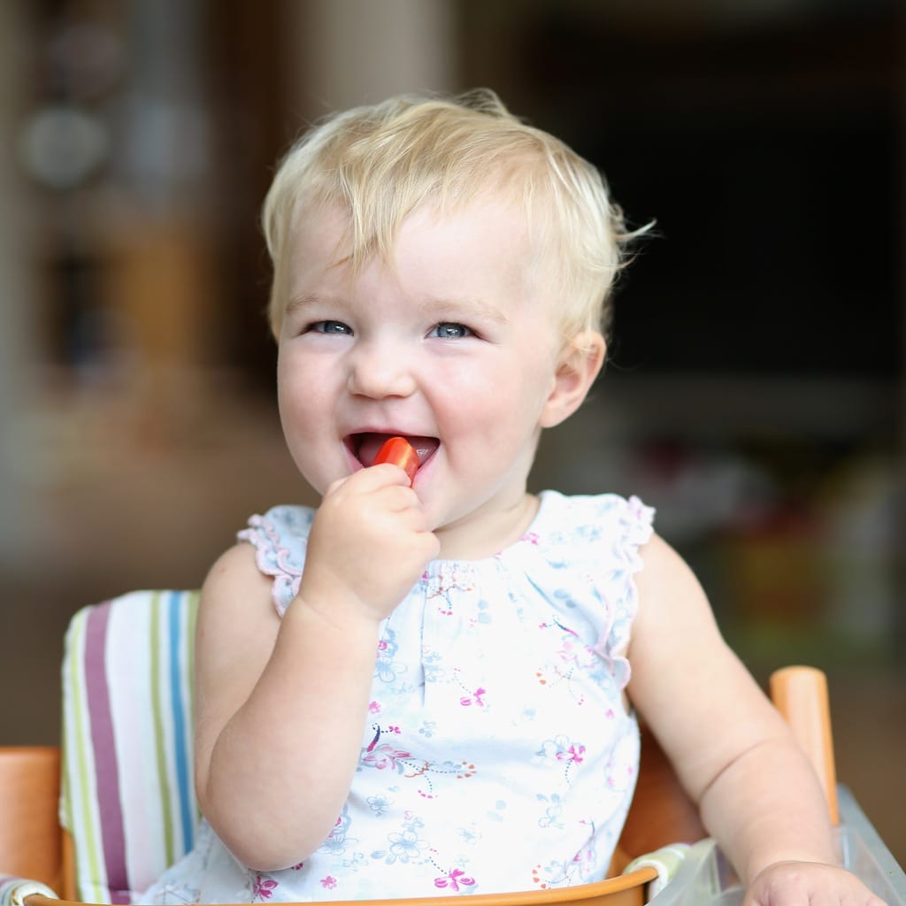 girl in highchair outside eating a strawberry with her pincer grasp
