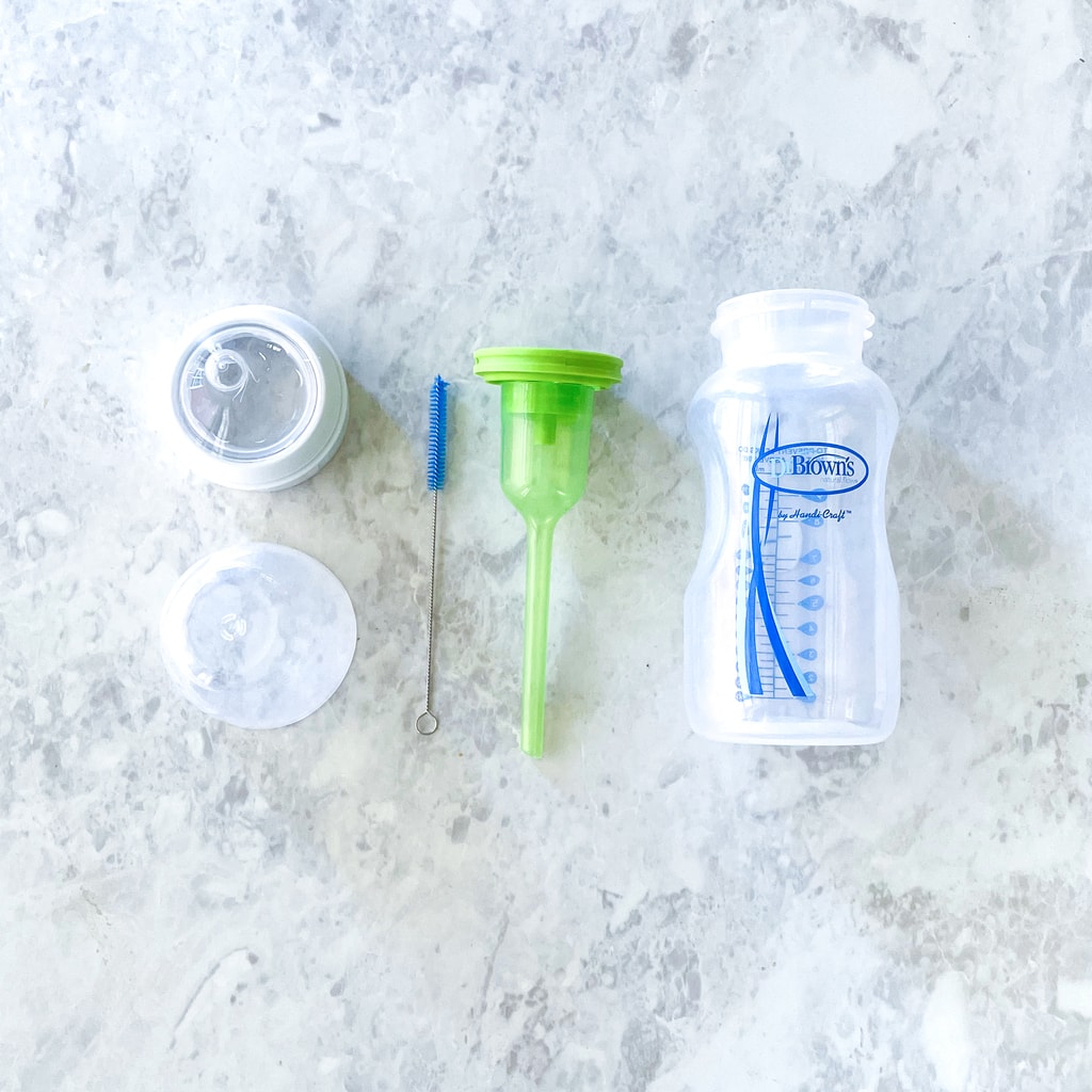 Is assembled bottle with the bottle, lead, nipple, flow indicator, and cleaning brush on a marble countertop.