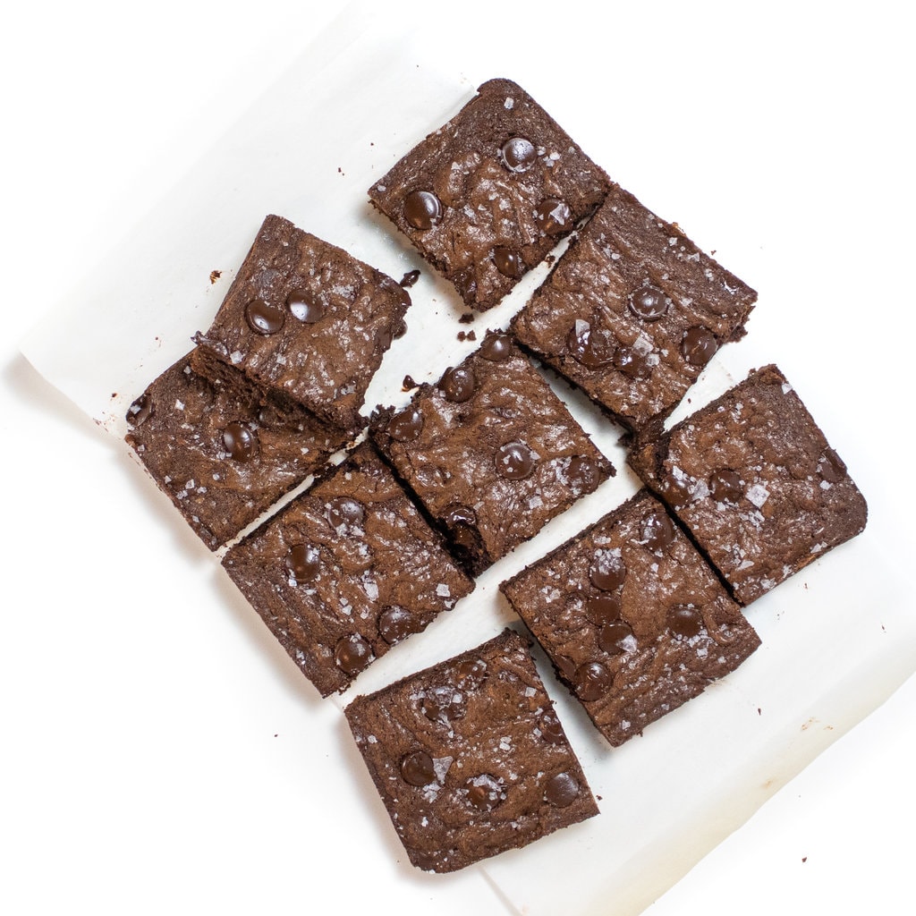 Nine brownies for lactation askew on white parchment paper against a white background.