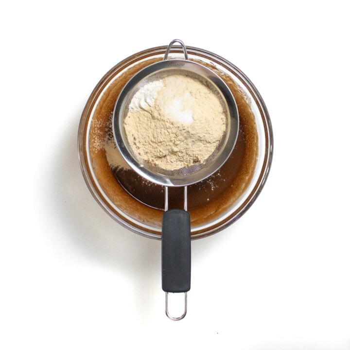 A glass bowl with a flour sifter on top with the dry ingredients in it.