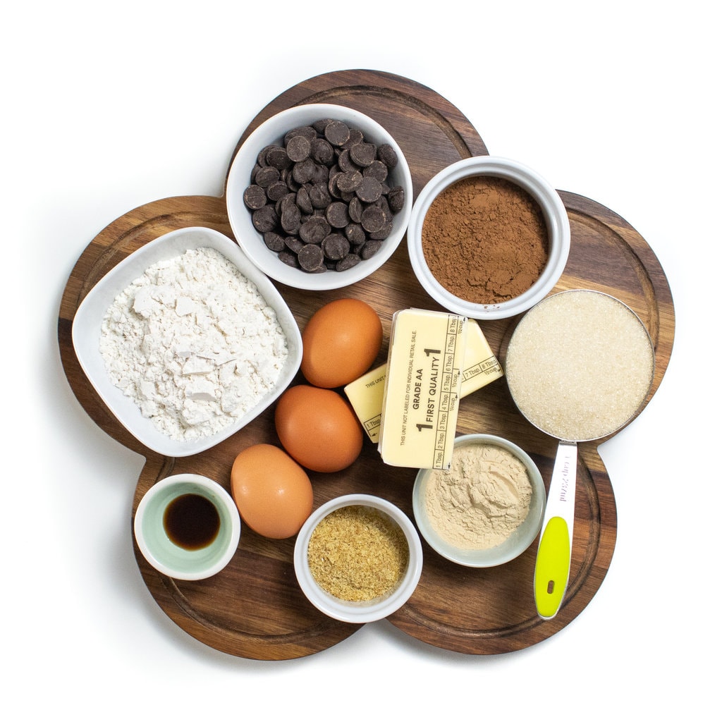 A wooden cutting board with ingredients in small bowls for lactation brownies.