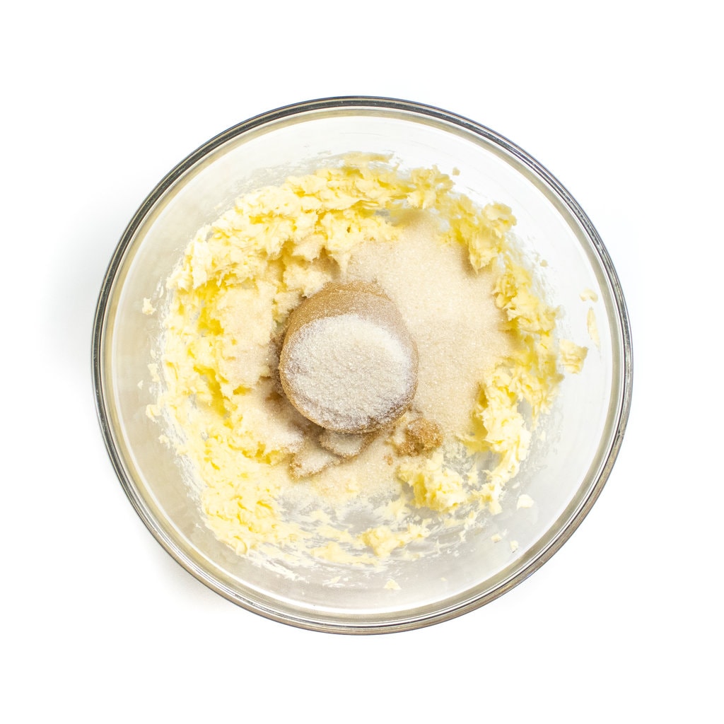 A glass mixing bowl with butter brown sugar and regular sugar.