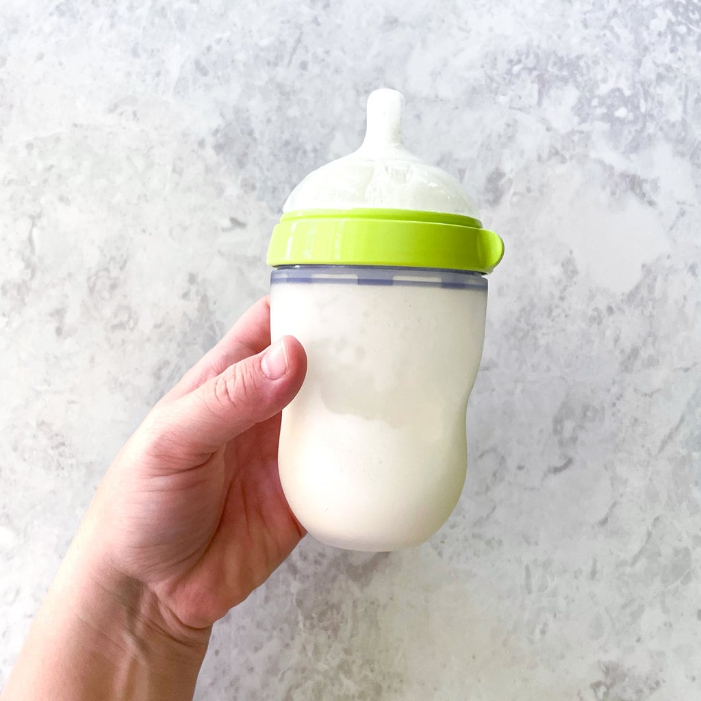 a comotomo bottle full of formula with a hand holding it against a marble countertop.