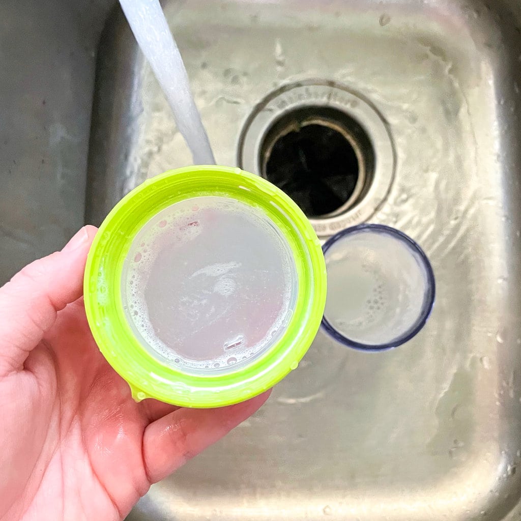 Hand holding the comotomo lid in a sink and washing it.