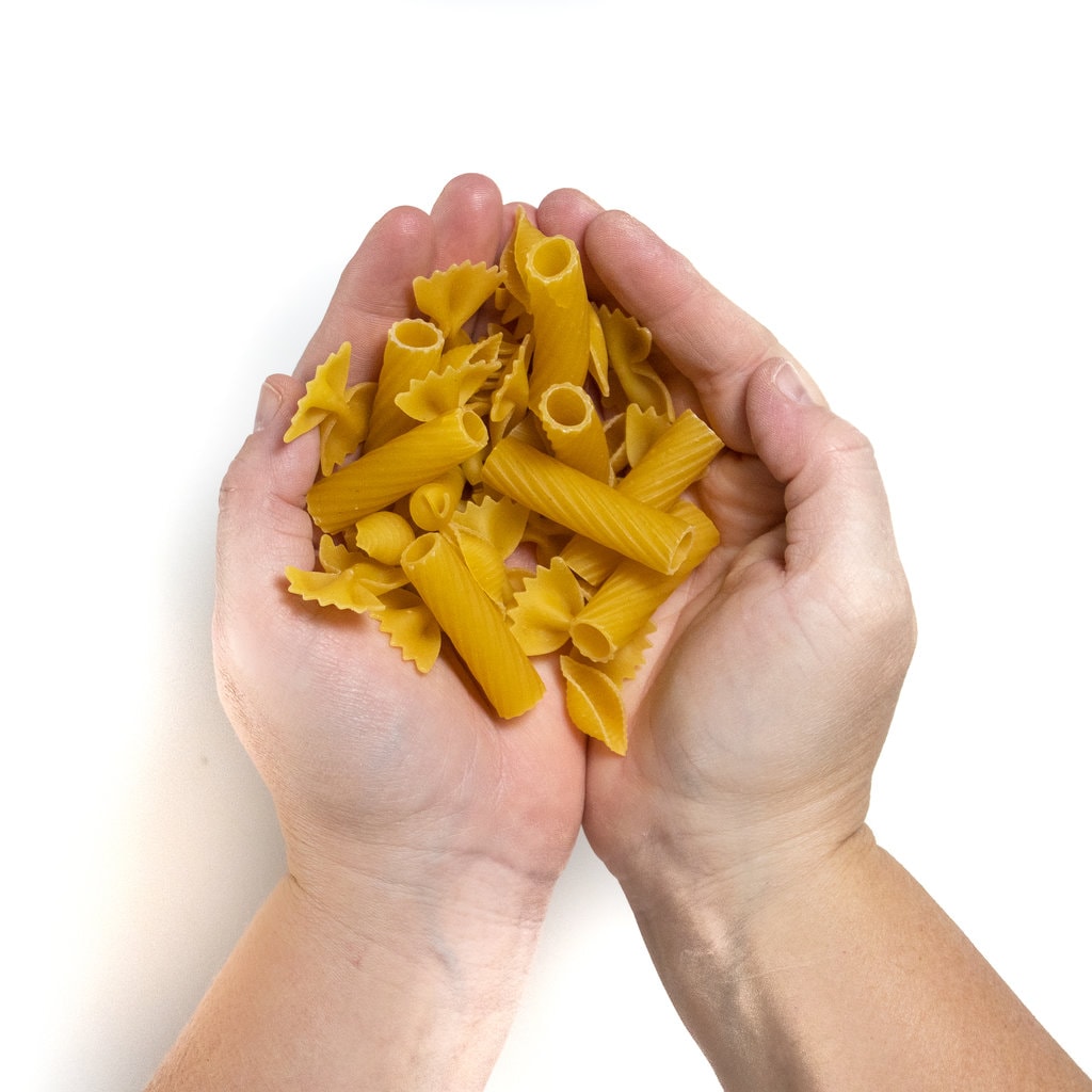 Hands holding several different types of dry pasta.