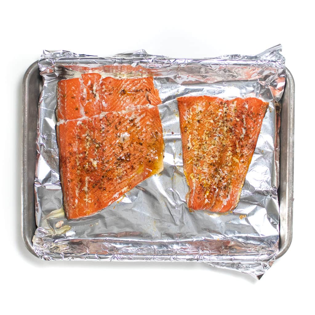 2 salmon fillets on a baking sheet that is covered in foil, baked in the oven.
