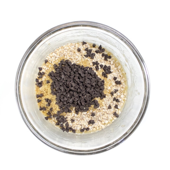 Clear bowl full of mashed banana instant oats and chocolate chips.