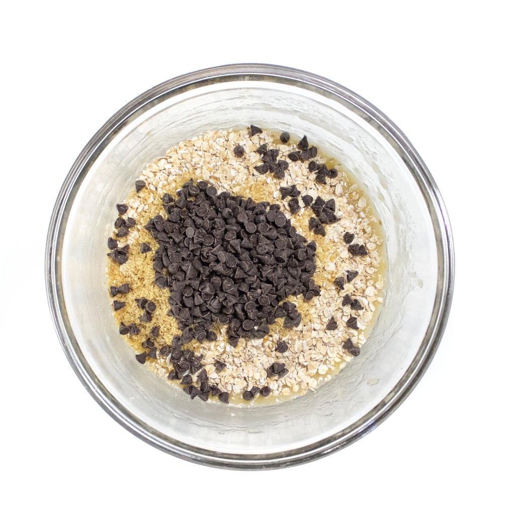 Clear bowl full of mashed banana instant oats and chocolate chips.